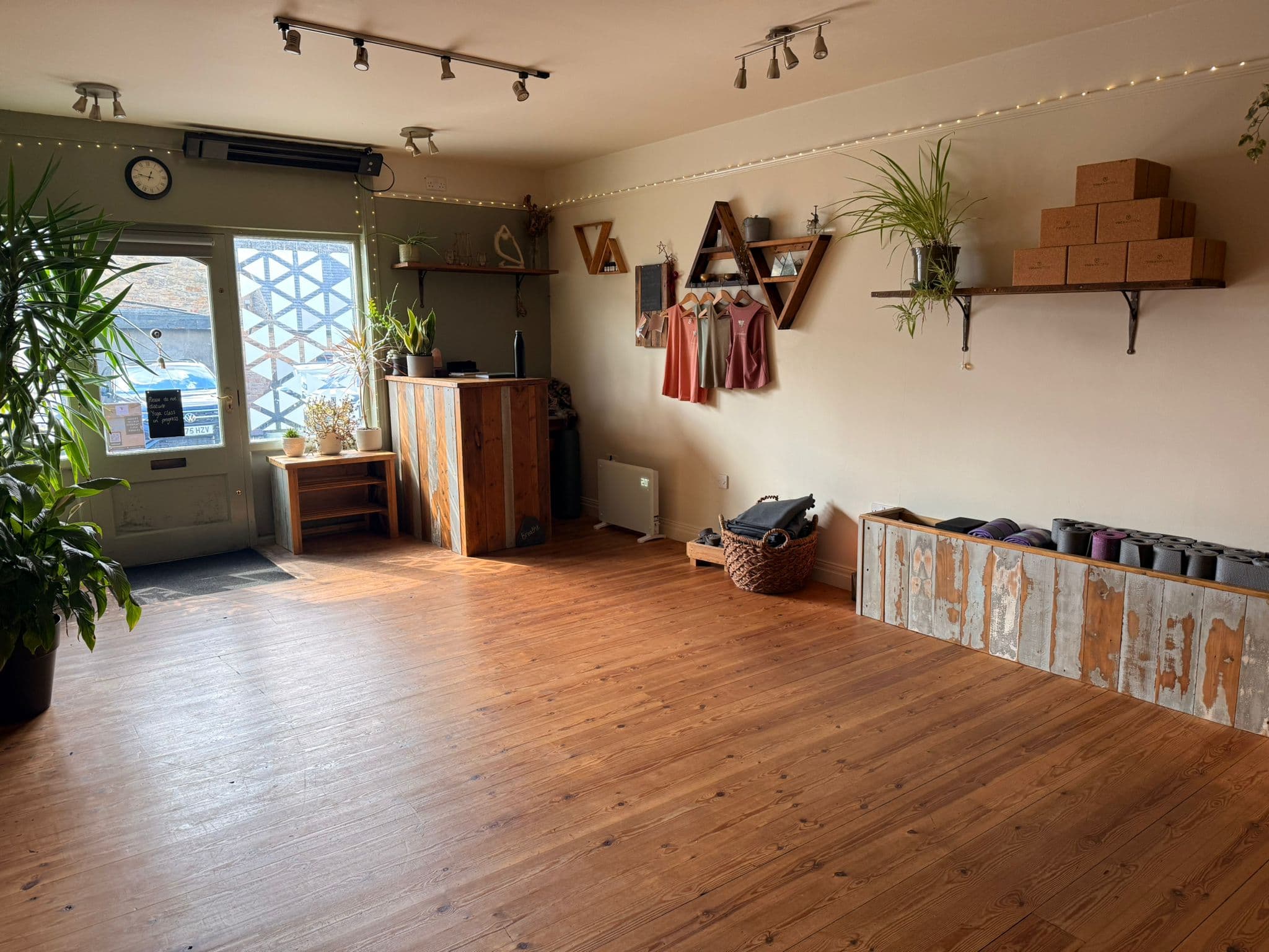 A beautiful yoga studio, with wooden floors, green plants and light flooding in through the windows.